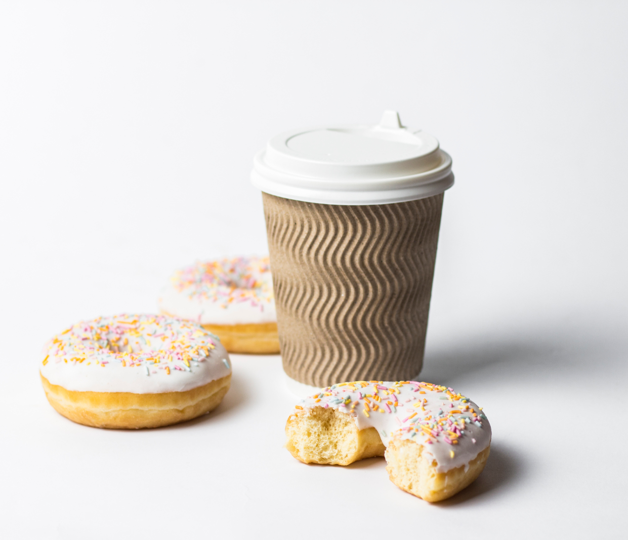 image shows a takeaway coffee, two donuts and one half eaten donut