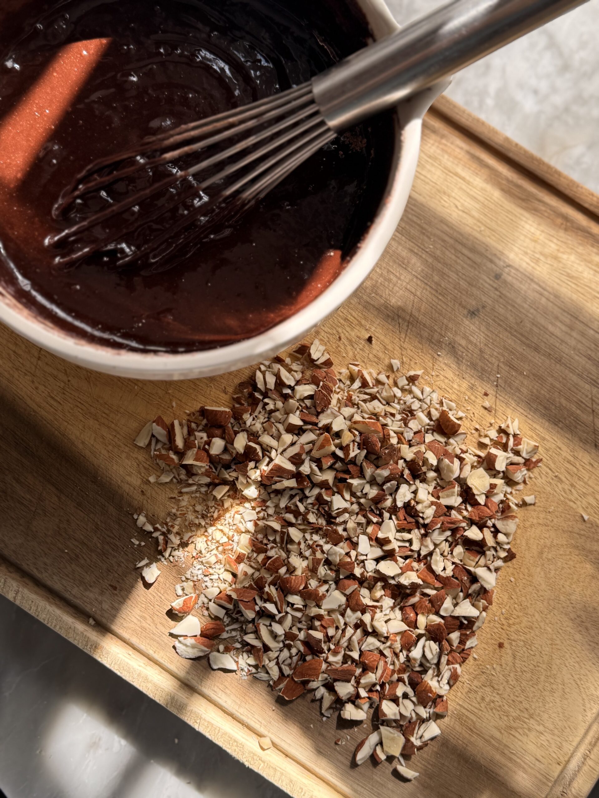 Brownie batter mix with a whisk, on a cutting board with chopped pecans.